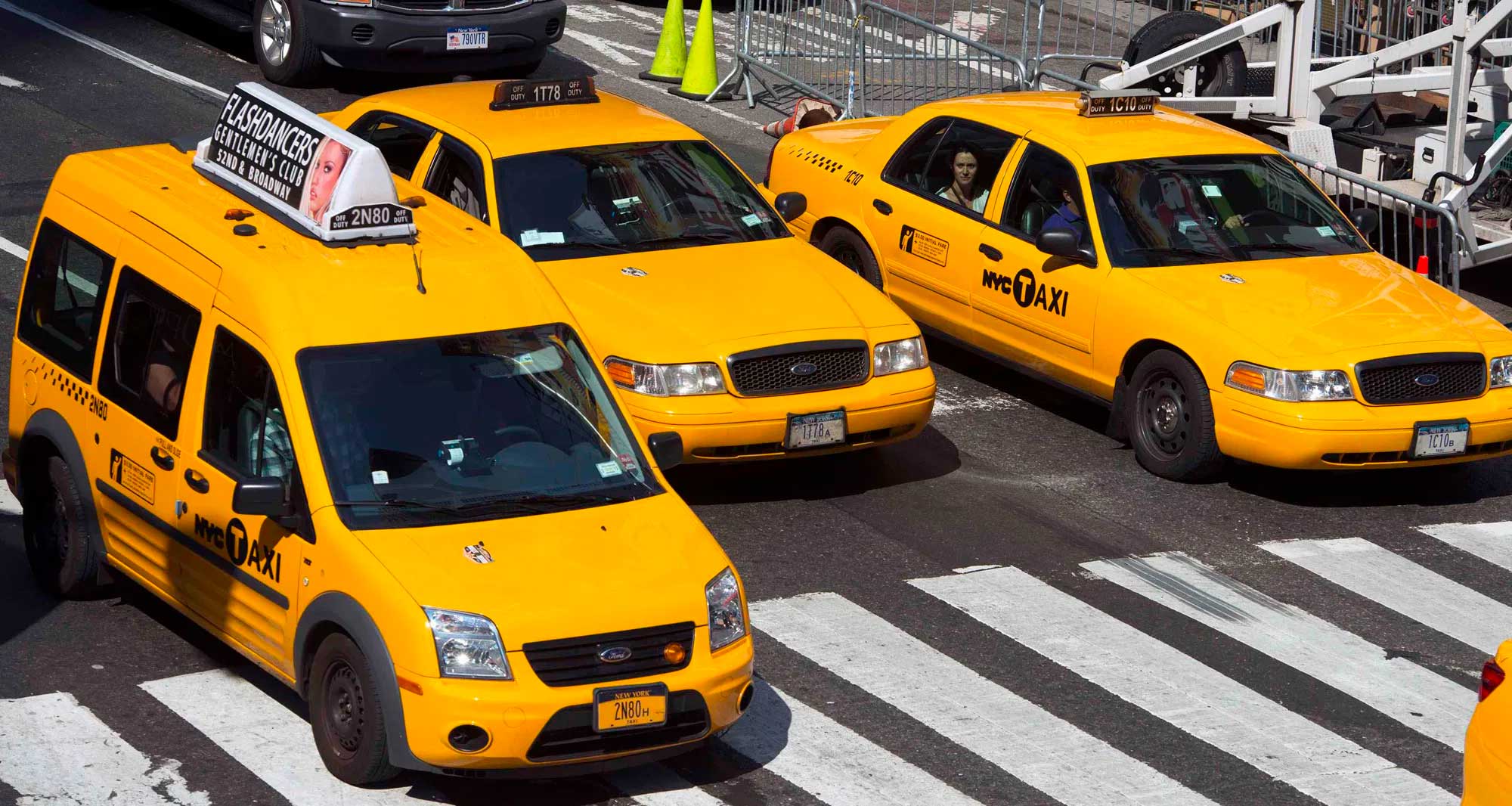 Three taxis stopped on the street at an intersection and crosswalk.