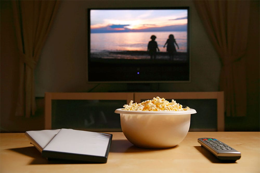 Photo Description: A living room TV, with DVDs, popcorn and a remote control on a coffee table in the foreground.