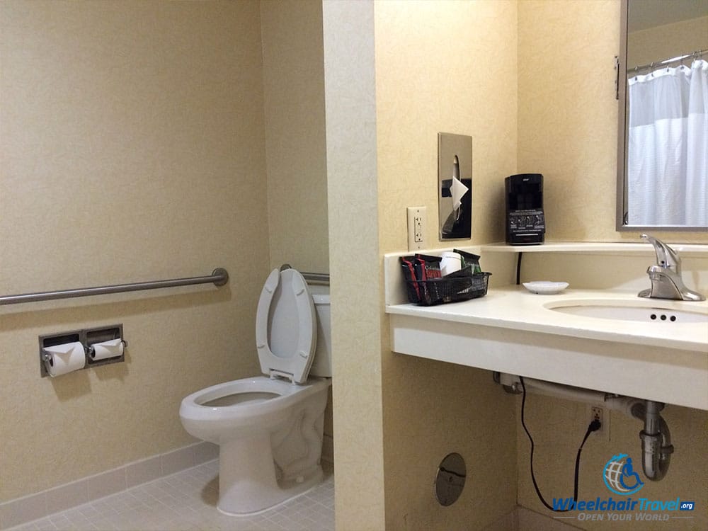 PHOTO DESCRIPTION: Bathroom toilet surrounded by grab bars, separated from the sink by a small wall.