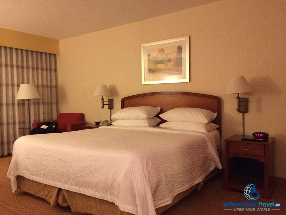 PHOTO DESCRIPTION: King size bed with white bed linens, with two nightstands, one on each side of the bed, and a chair in the far distance.