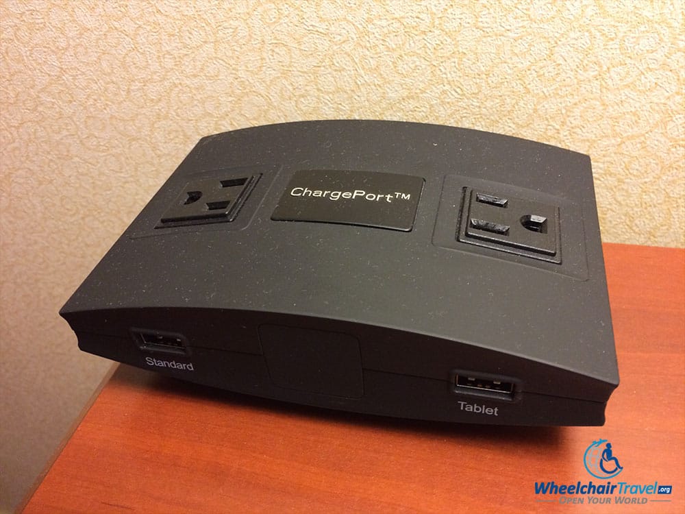 PHOTO DESCRIPTION: A power charging station sat atop the nightstand on the left of the bed, with two AC power outlets and two USB charging ports.