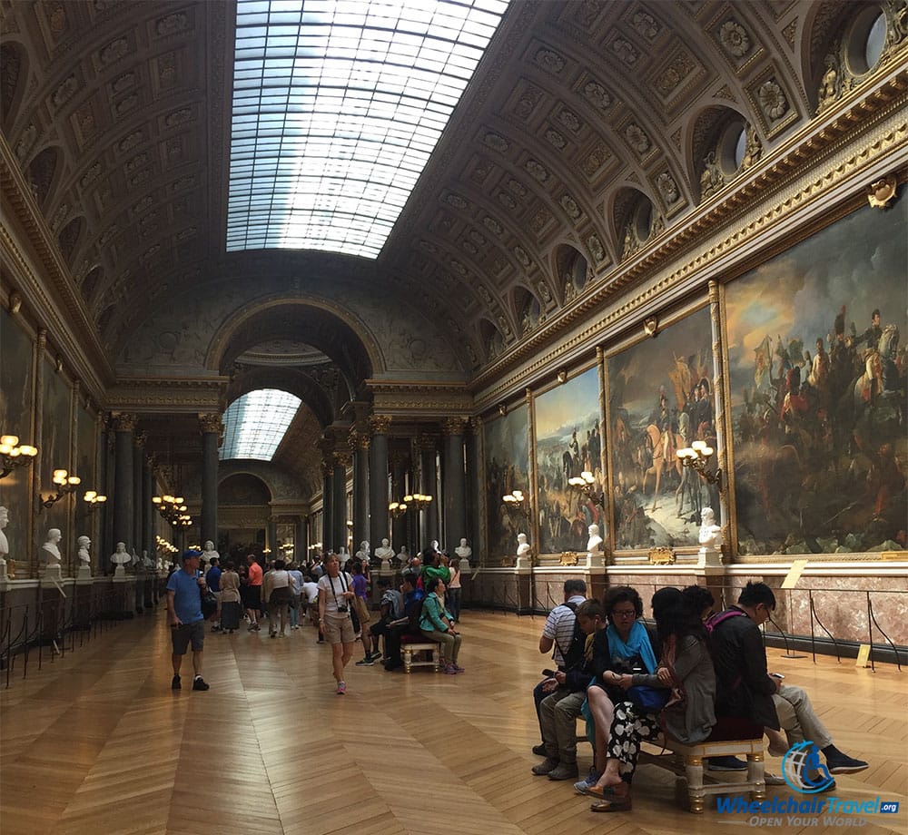 PHOTO DESCRIPTION: A long hall with a partially glass ceiling, with massive paintings on either side.