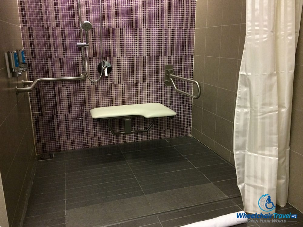 PHOTO DESCRIPTION: Roll-in shower with grab bars and seat affixed to wall.