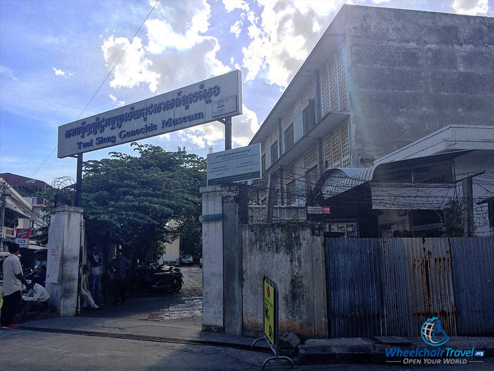 PHOTO DESCRIPTION: Walled property, with a gate on a street corner opened to the museum. Sign above the gate reads TUOL SLENG GENOCIDE MUSEUM.