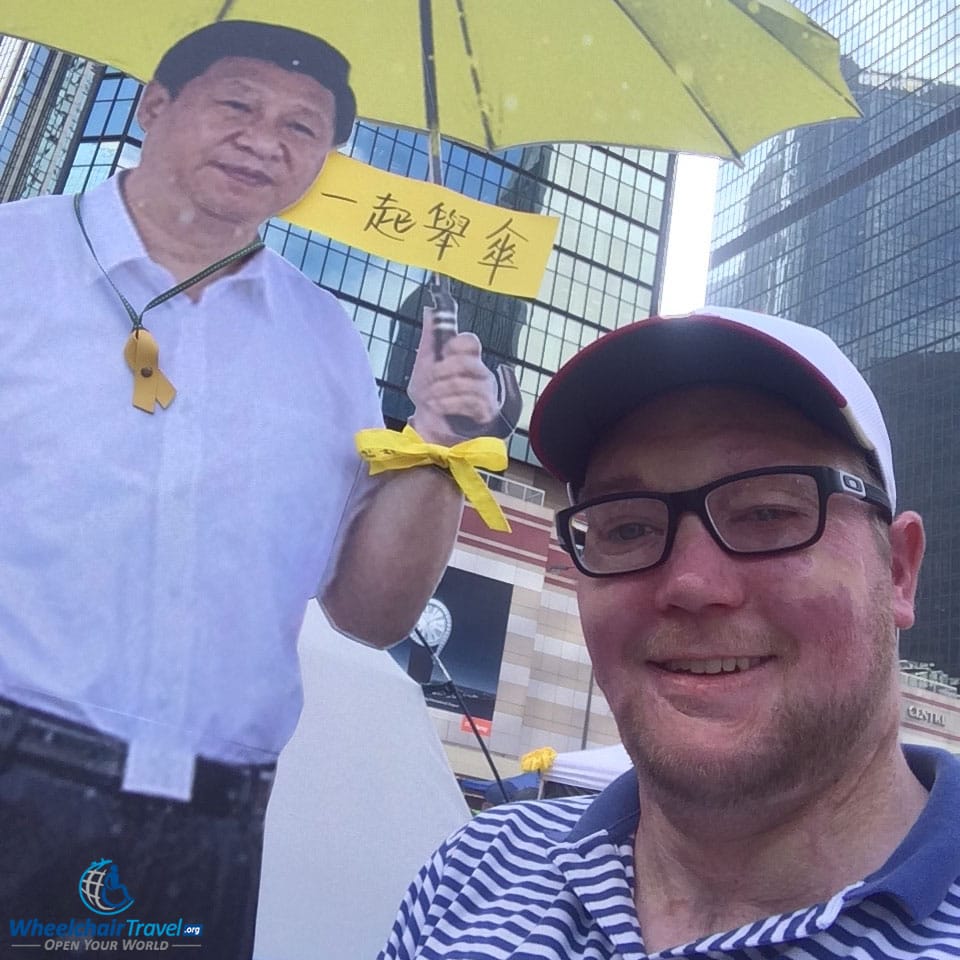 PHOTO DESCRIPTION: Selfie with a cardboard cutout of Chinese President Xi Jinping, holding a yellow umbrella.