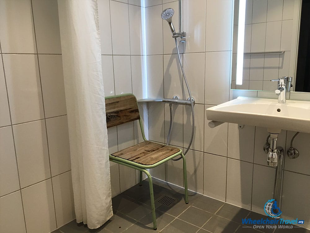 Roll-in shower with chair at Urban House Hostel.