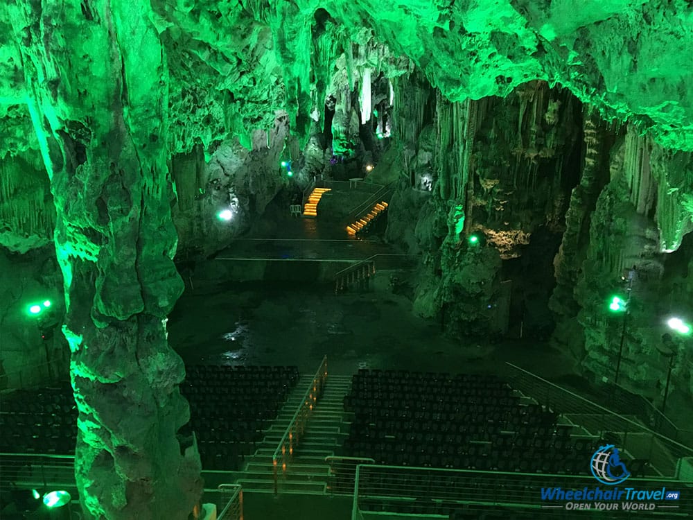 Large cave, with auditorium chairs and seats, lit in a glow of green light.