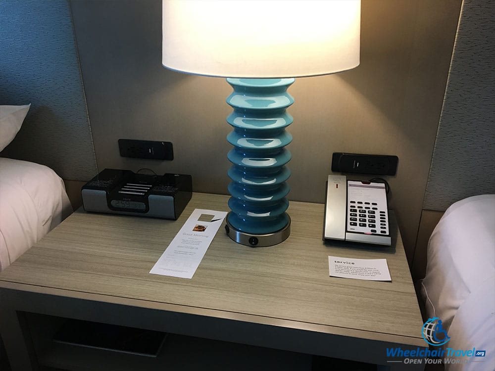 Nightstand with a telephone, alarm clock and lamp.