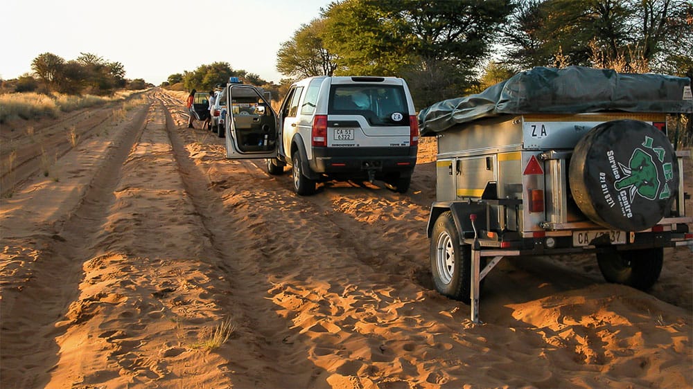 Land Rover with travel trailer parked along a sandy road in Africa