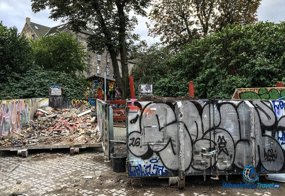 Graffiti on a trash dumpster, with a beautiful home in the background.