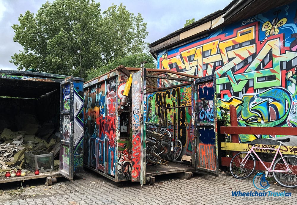 Graffiti painted on the side of a building, spilling over onto a dumpster.