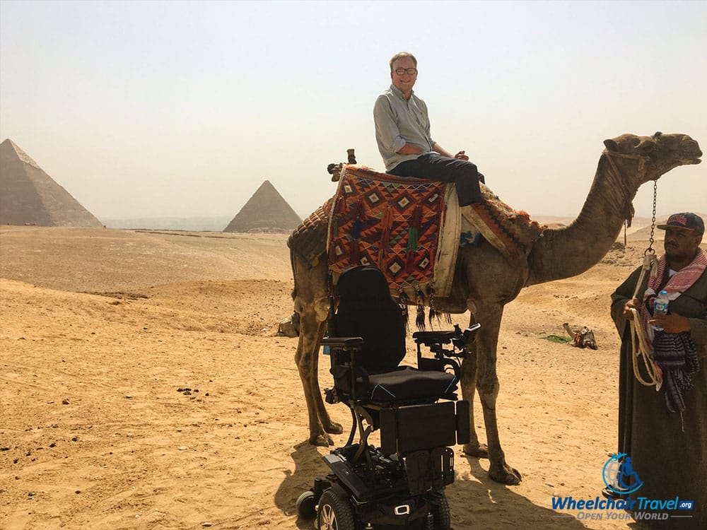 Quantum Q6 Edge 2.0 power wheelchair next to John, sitting on a camel's back.