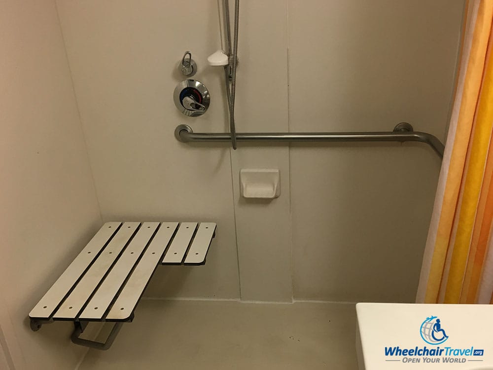 Wheelchair accessible roll-in shower with a folding seat attached to the wall.