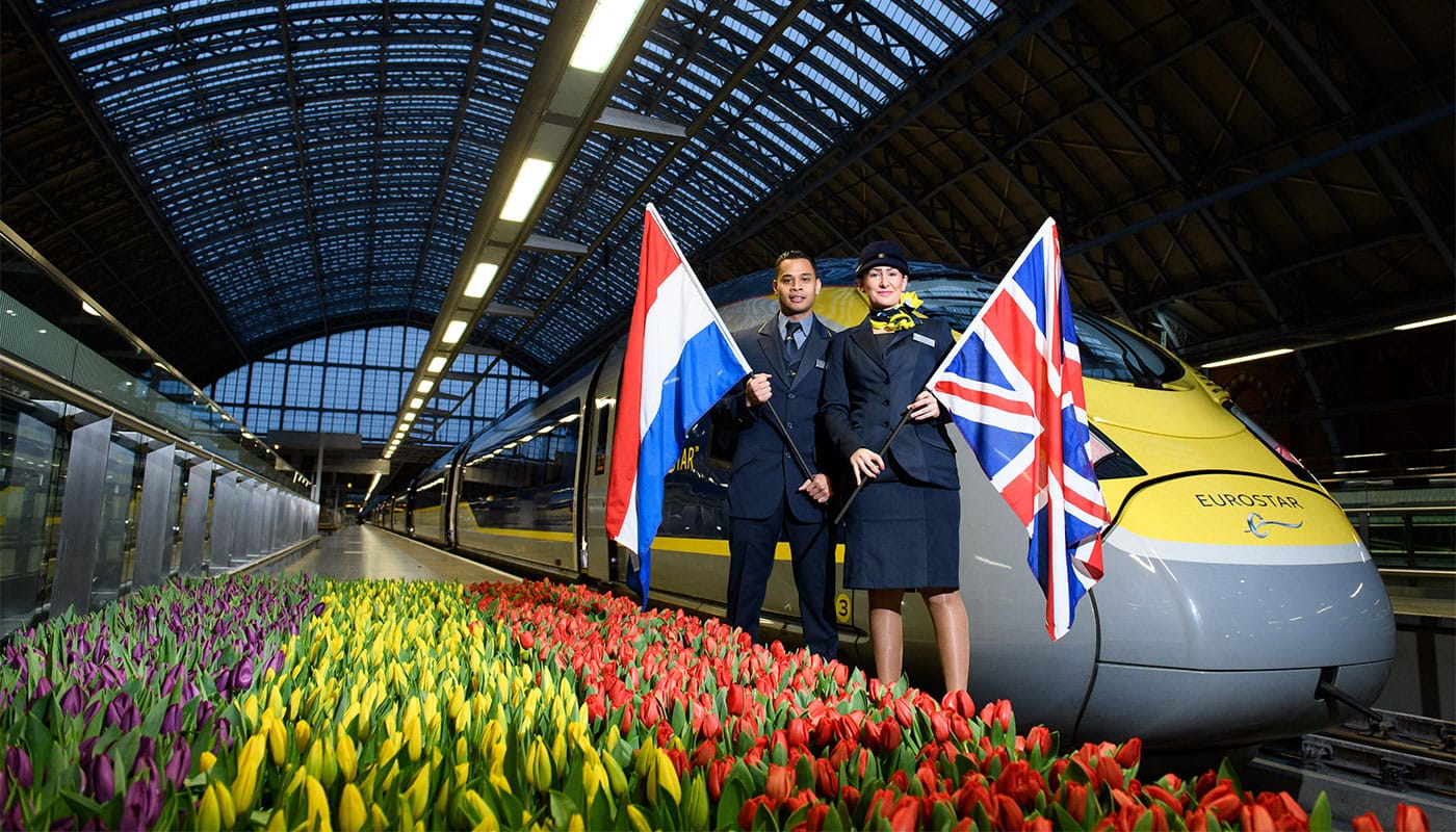 Eurostar staff standing next to train holding flags of the United Kingdom and Netherlands.