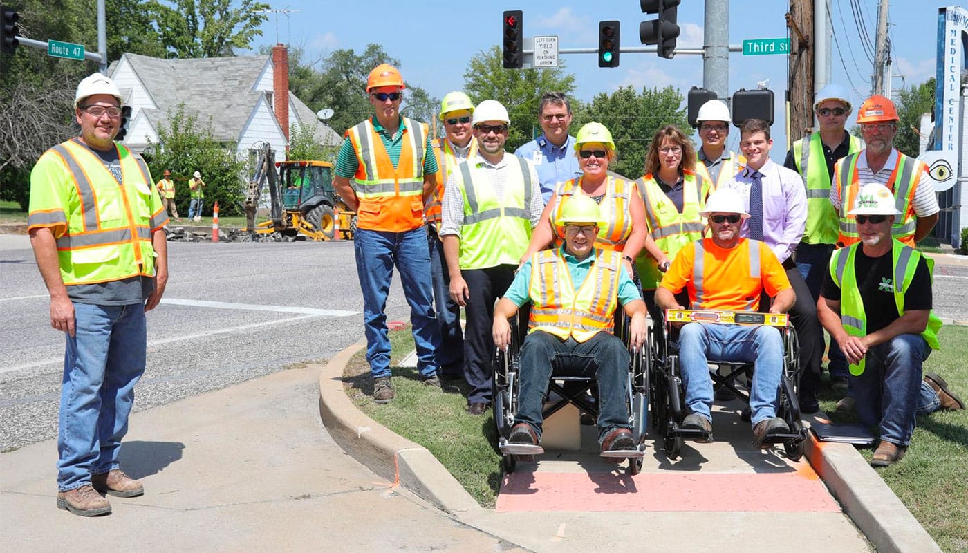 Road construction crews at a sidewalk curb cut, testing out a wheelchair.