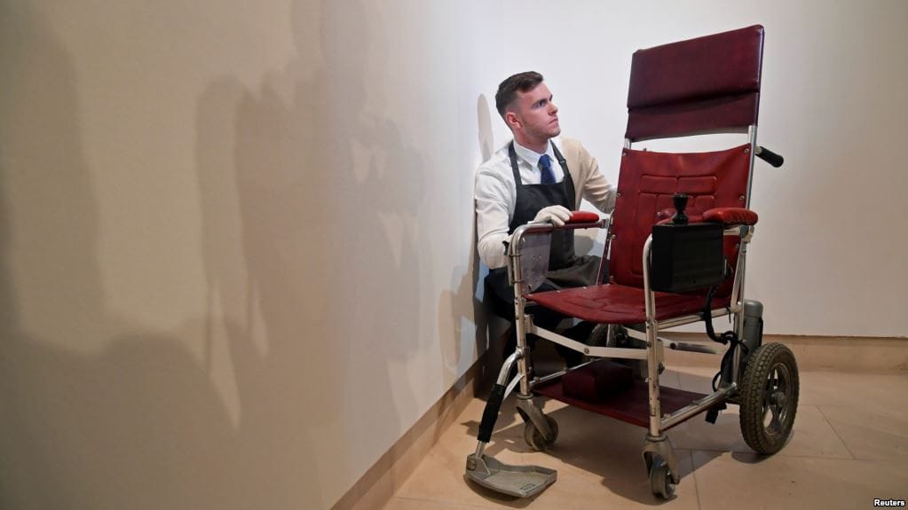 Fine-art handler Tom Richardson poses with a motorized wheelchair belonging to British theoretical physicist Stephen Hawking ahead of an auction of items from Hawkings' personal estate at Christie's in London, Oct. 30, 2018. | Photo courtesy Reuters/VOA News.