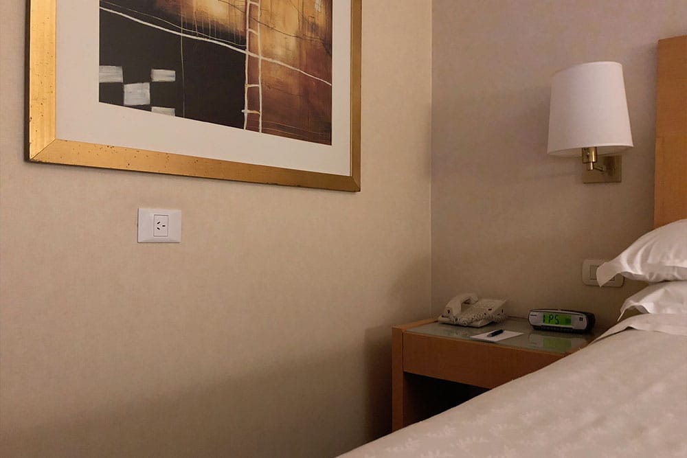 Power outlet on wall parallel to the bed.