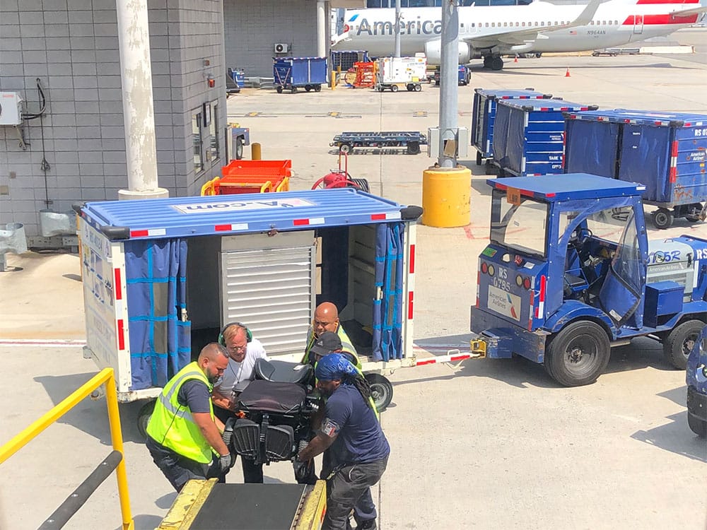 American Airlines baggage handlers lifting wheelchair at JFK Airport.