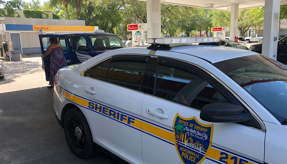 Police cruiser and wheelchair taxi at gas station.