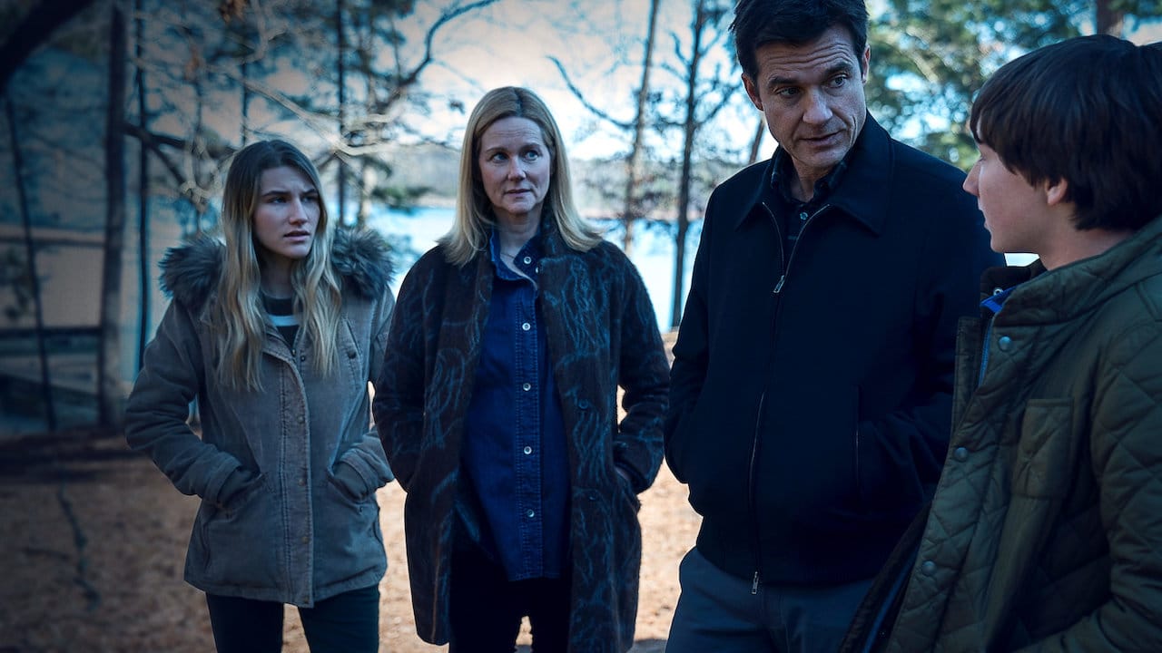 A man and woman stand alongside a lake with their teenage daughter and son.