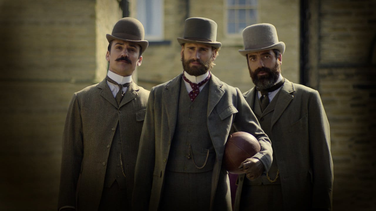 Three English men wearing suits and top hats pose; one man holds a football.