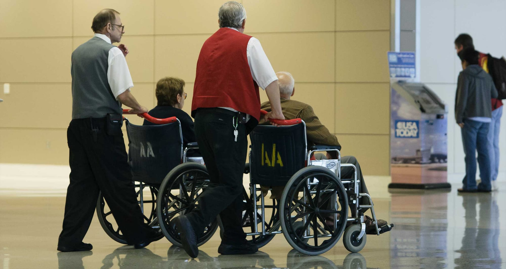 Two airline staff members pushing wheelchairs through the airport terminal.