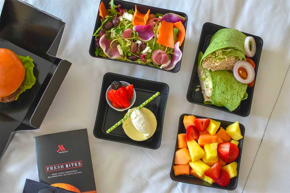 Salads, wraps, fruit and a burger laid out on a bed in Fresh Bites containers.