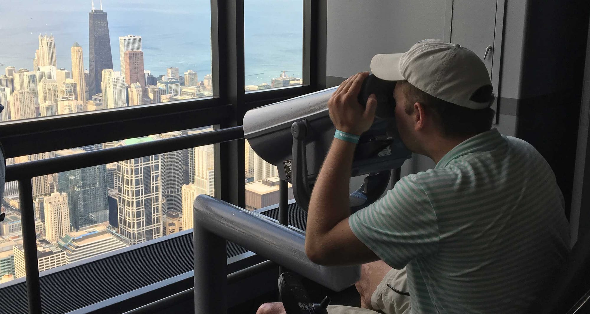 Wheelchair user looking through an accessible viewfinder towards a city skyline.