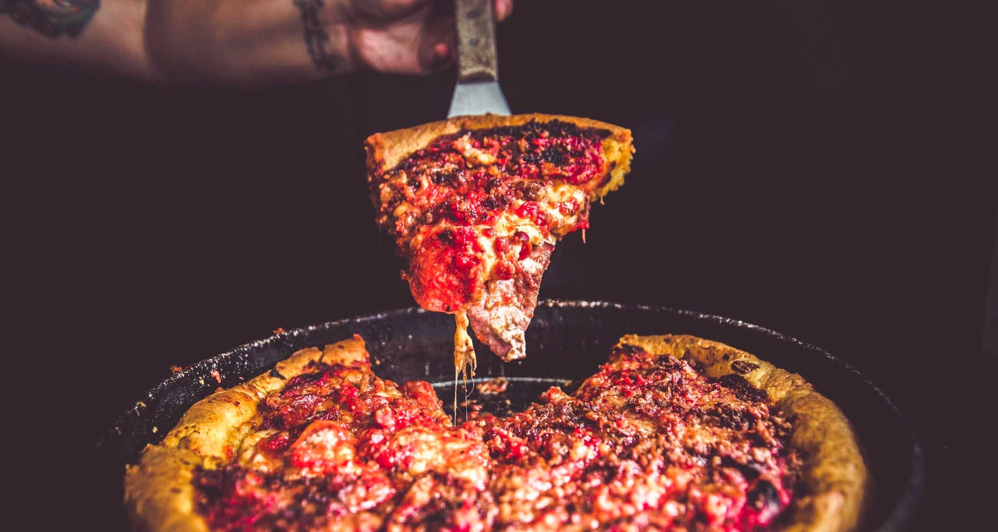 Slice of deep dish pizza being lifted from the whole pie.