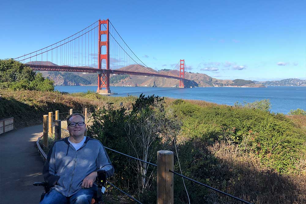 John seated in his wheelchair, with the Golden Gate Bridge in the background.