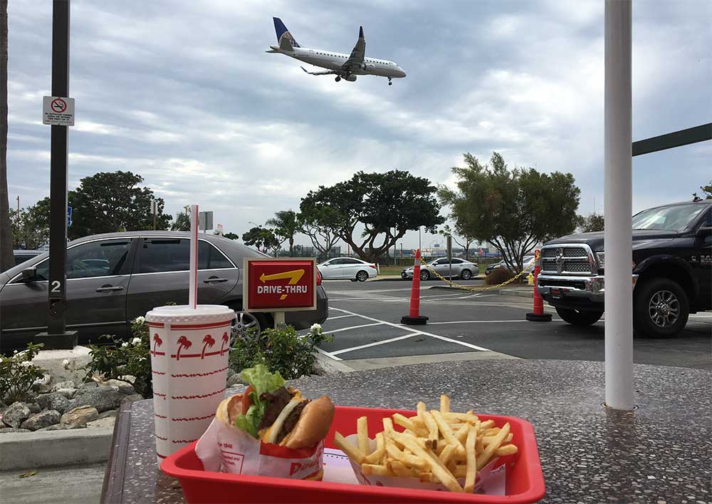 Fast food meal on a picnic table outside; airplane landing in the background.