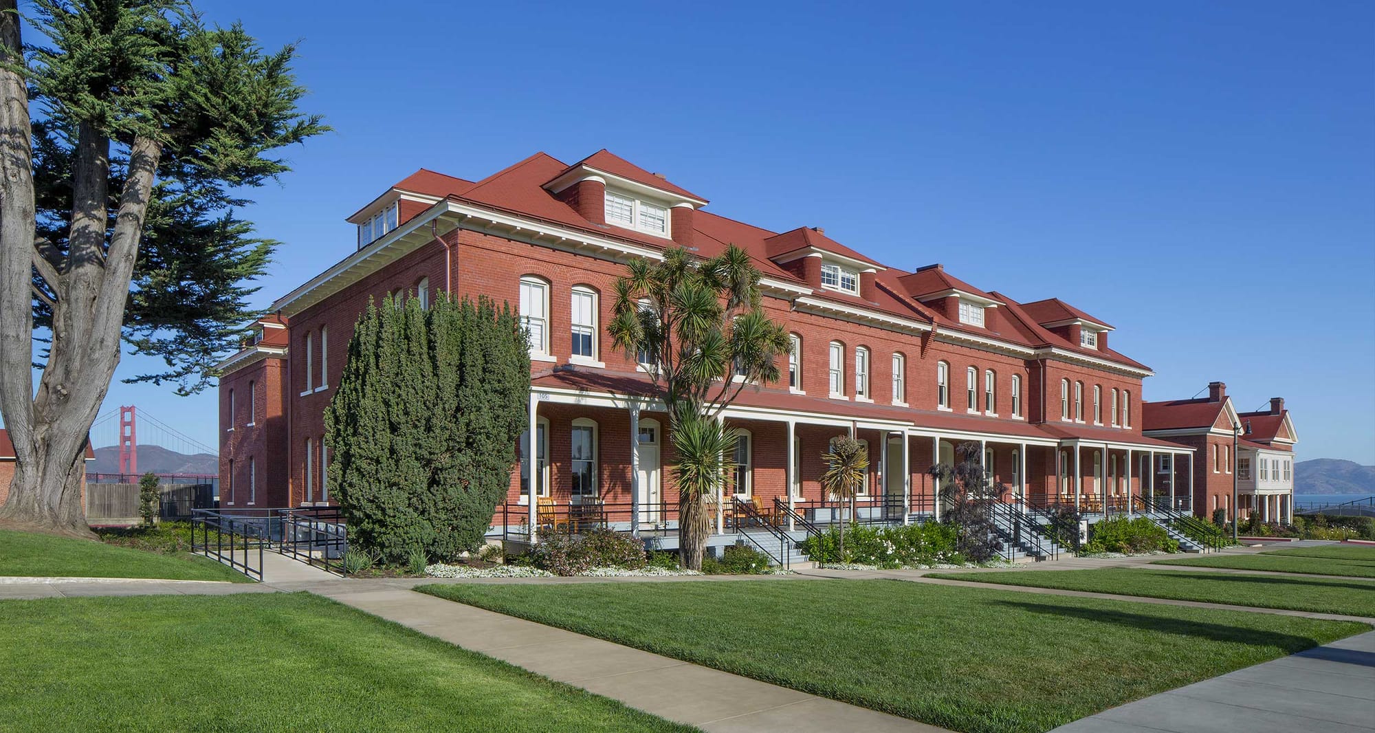 Exterior of The Lodge at the Presidio, a three story brick building sitting in front of the Golden Gate Bridge.