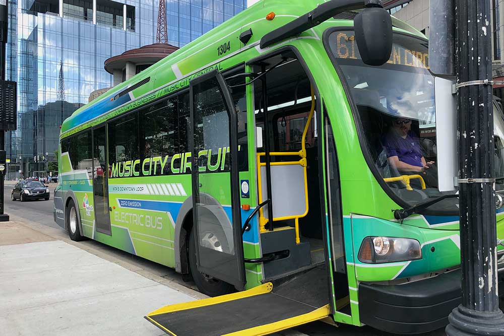 Green colored city bus with wheelchair ramp extended onto sidewalk.