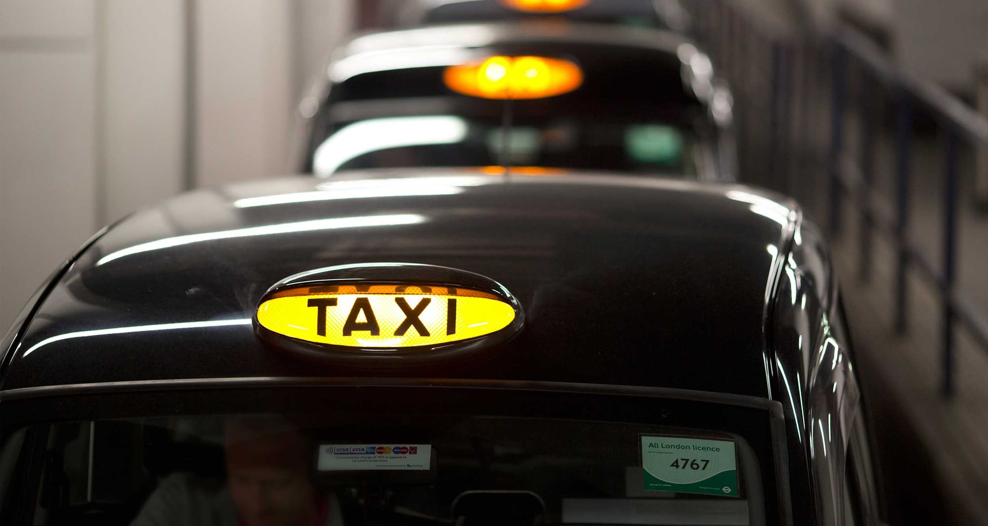 Row of black wheelchair accessible cans with a yellow taxi badge on the rooftop.