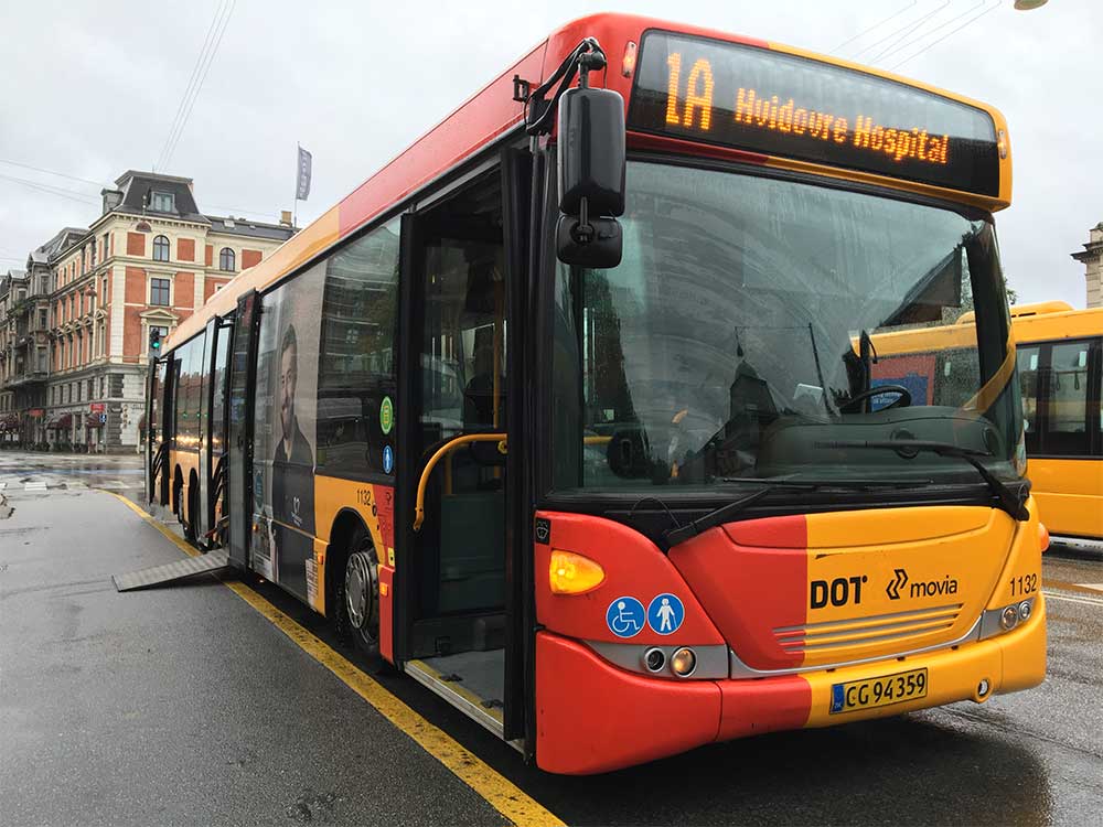 Elongated city bus, with wheelchair ramp deployed onto sidewalk.