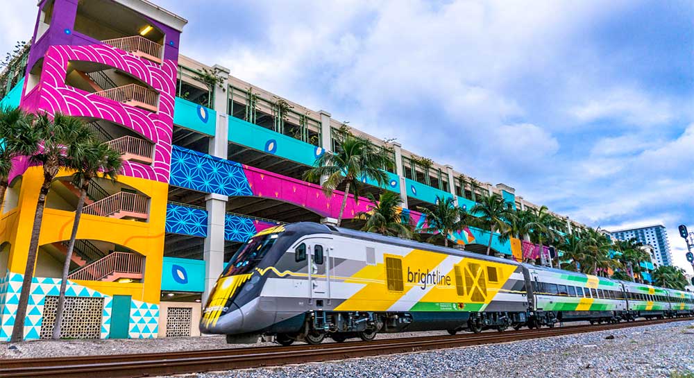 Brightline train passing in front of colorfully painted parking garage in South Florida.