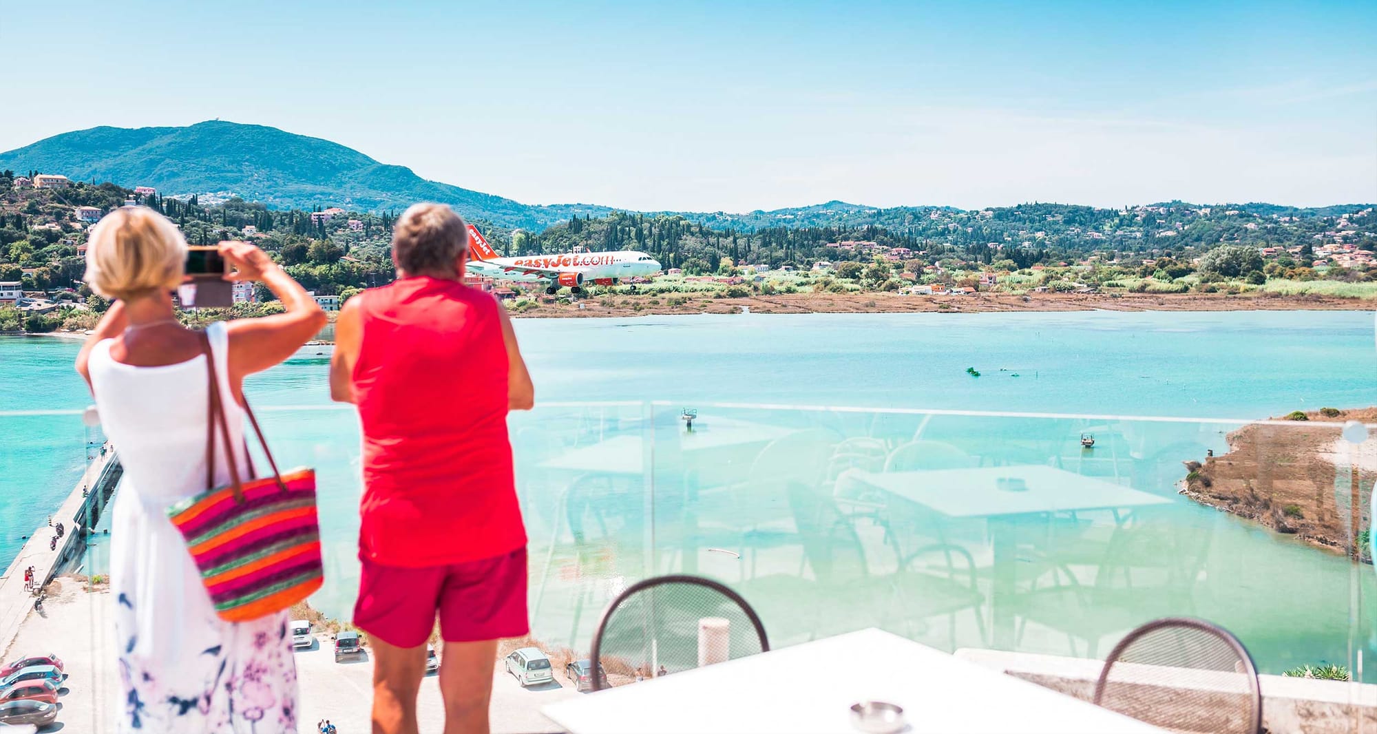 Older couple taking a photo of an airplane flying over a beach.