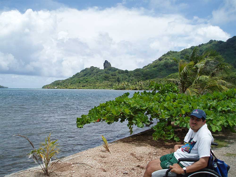 Gordon posing for a photo along the water with a lush tropical background.