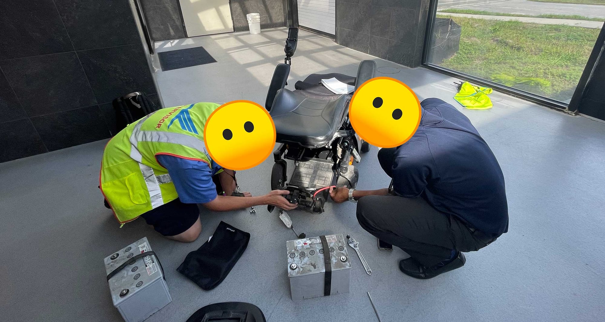 Two airline staff persons disassembling a power wheelchair with batteries removed.