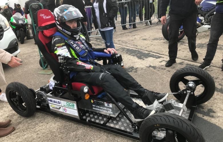 Man seated on four-wheeled chair while wearing racing helmet.