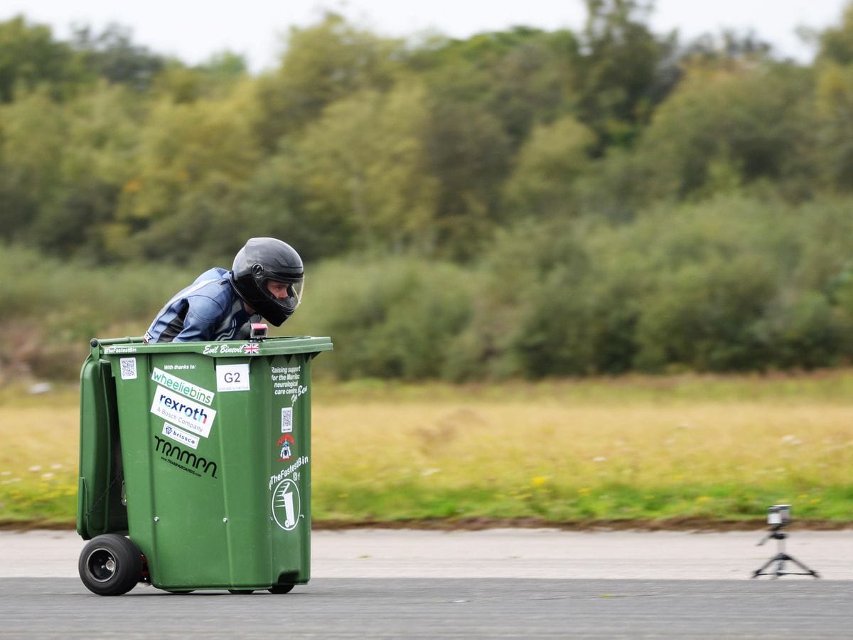 Man crouched in garbage bin while wearing a helmet.