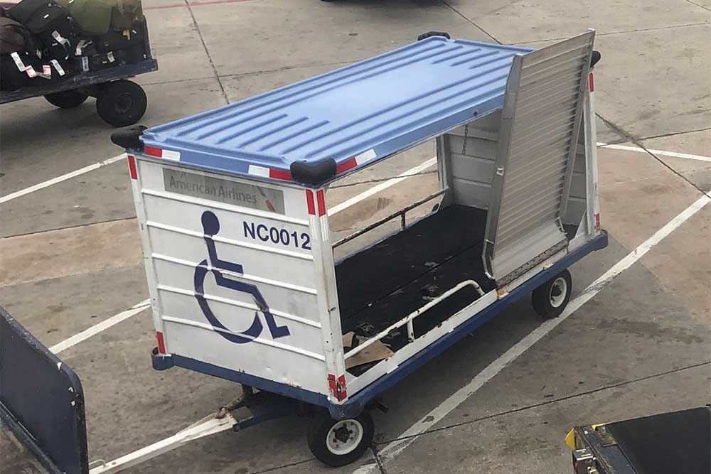 Airline baggage cart with a folding ramp attached to the side. Wheelchair icon painted on end of cart.