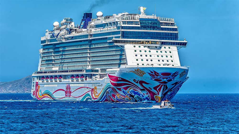 Large white cruise ship on the water, led by a tug boat.