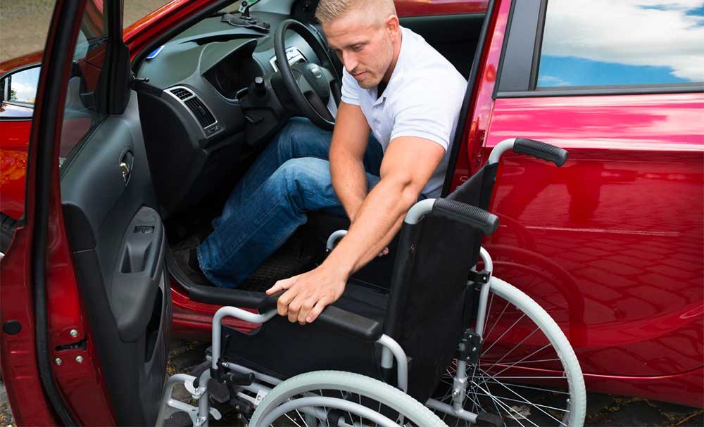 Wheelchair user transferring into a red car.