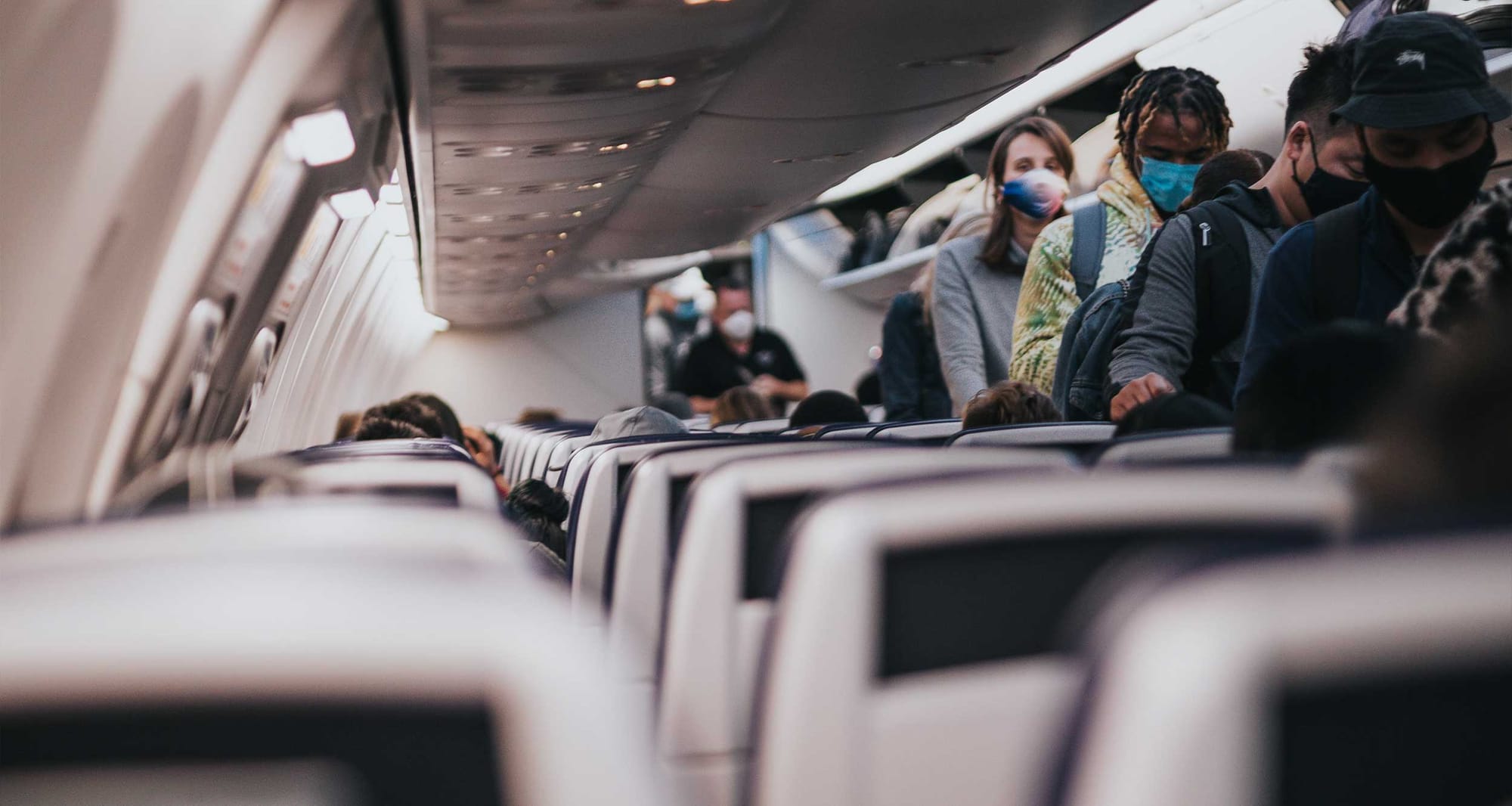 People walking down aisle of airplane wearing face masks.