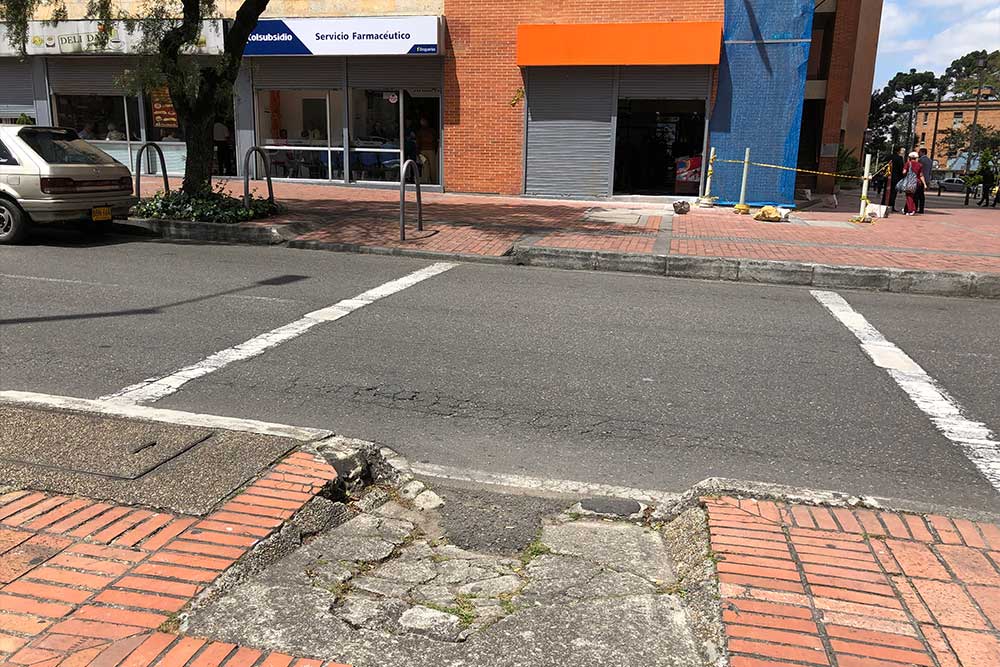 Curb ramp with potholes and cracked cement.