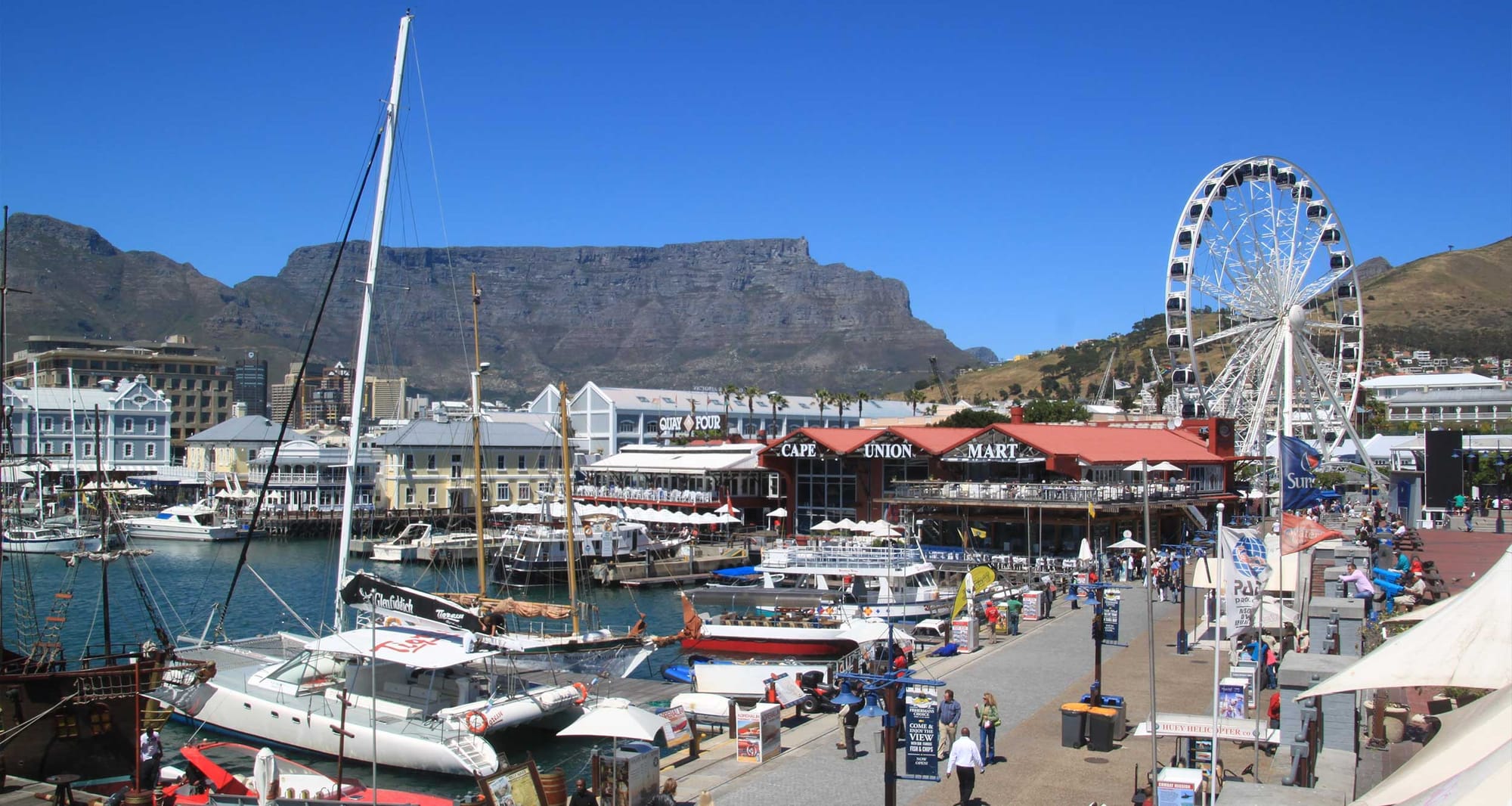 Cape Town boardwalk with Ferris wheel and mountain in background.