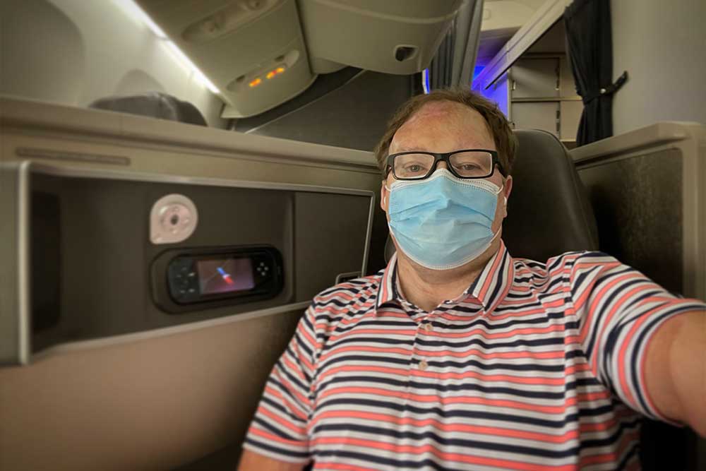 John wearing a face mask wile seated on an airplane seat.