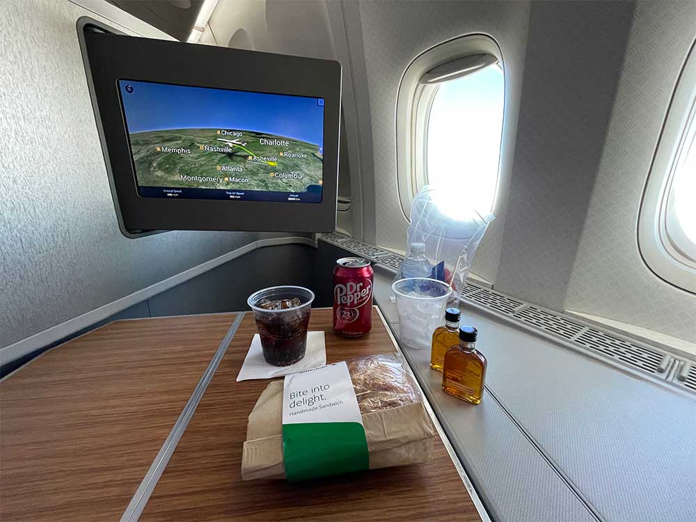 Sandwich, Dr. Pepper and a bourbon on an airplane tray table.