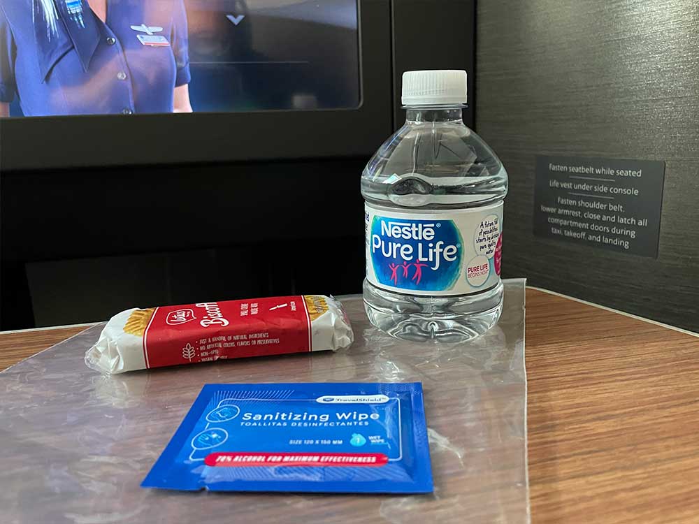 Plastic bag containing small bottled water, package of biscoff cookies and a sanitizer wipe.